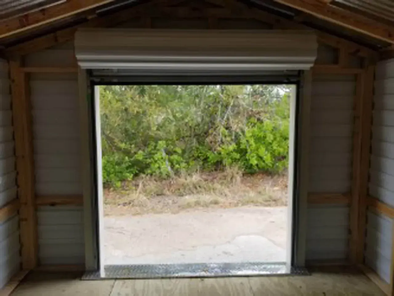 Interior of shed with a roll-up door open to a view of foliage.