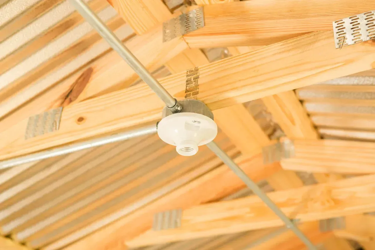 Exposed light fixture attached to a wooden roof frame. Metal conduit runs across the frame.