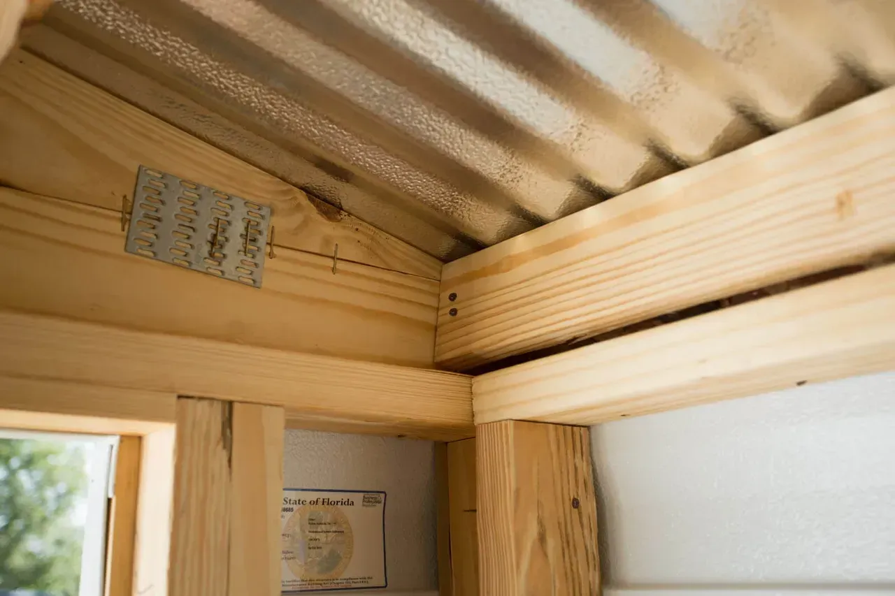 Interior corner of a wooden structure with corrugated metal roof and a metal bracket.
