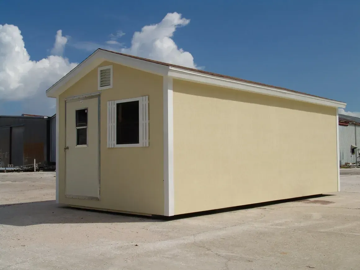 Beige rectangular building with white trim, door, and window. Brown roof, blue sky, and clouds.