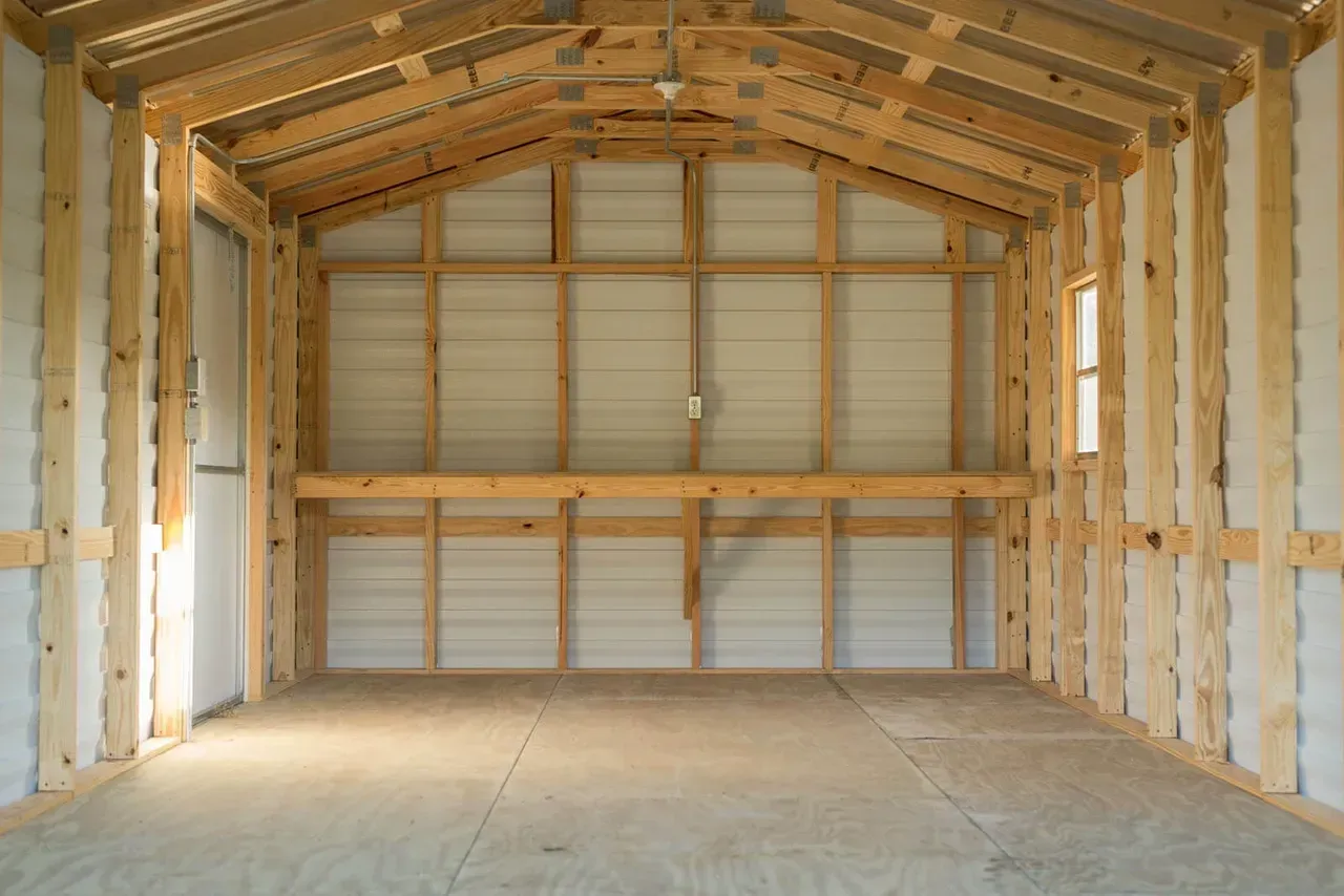 Empty interior of a wooden-framed shed, with metal siding and a shelf.