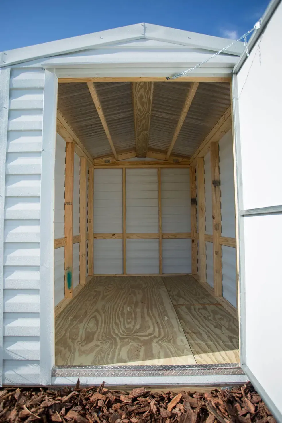 White metal storage shed with open door, showing wooden interior and floor.