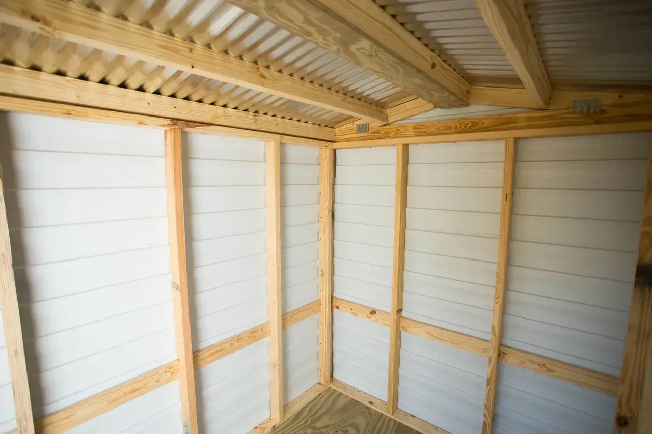 Interior view of a small wooden structure with white panel walls and a corrugated metal ceiling.