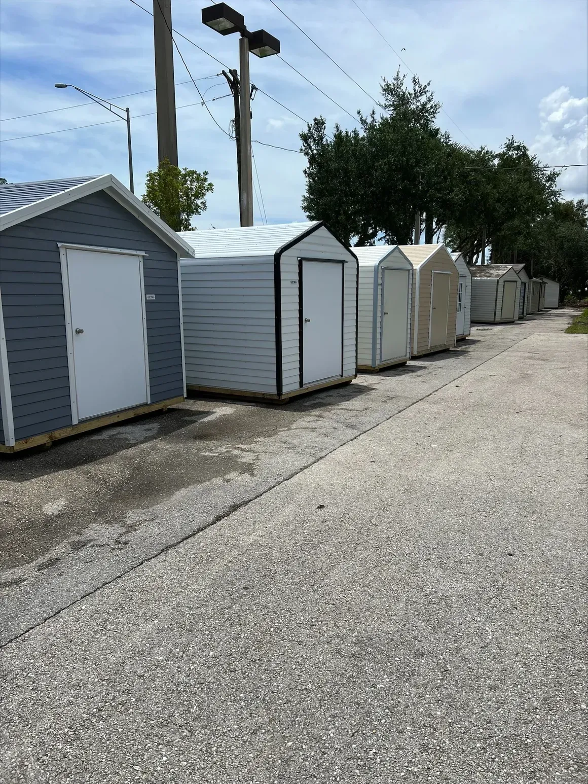 Row of storage sheds of various colors along an asphalt path under a cloudy sky.