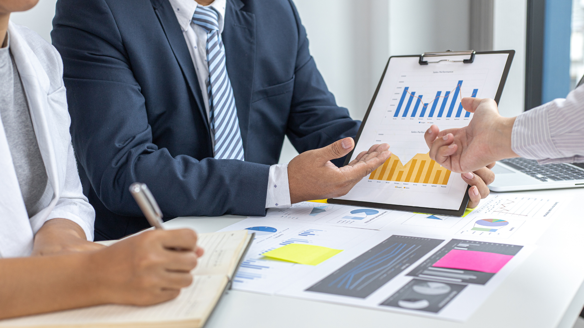 Business meeting with hands pointing at charts and a clipboard on a table with documents