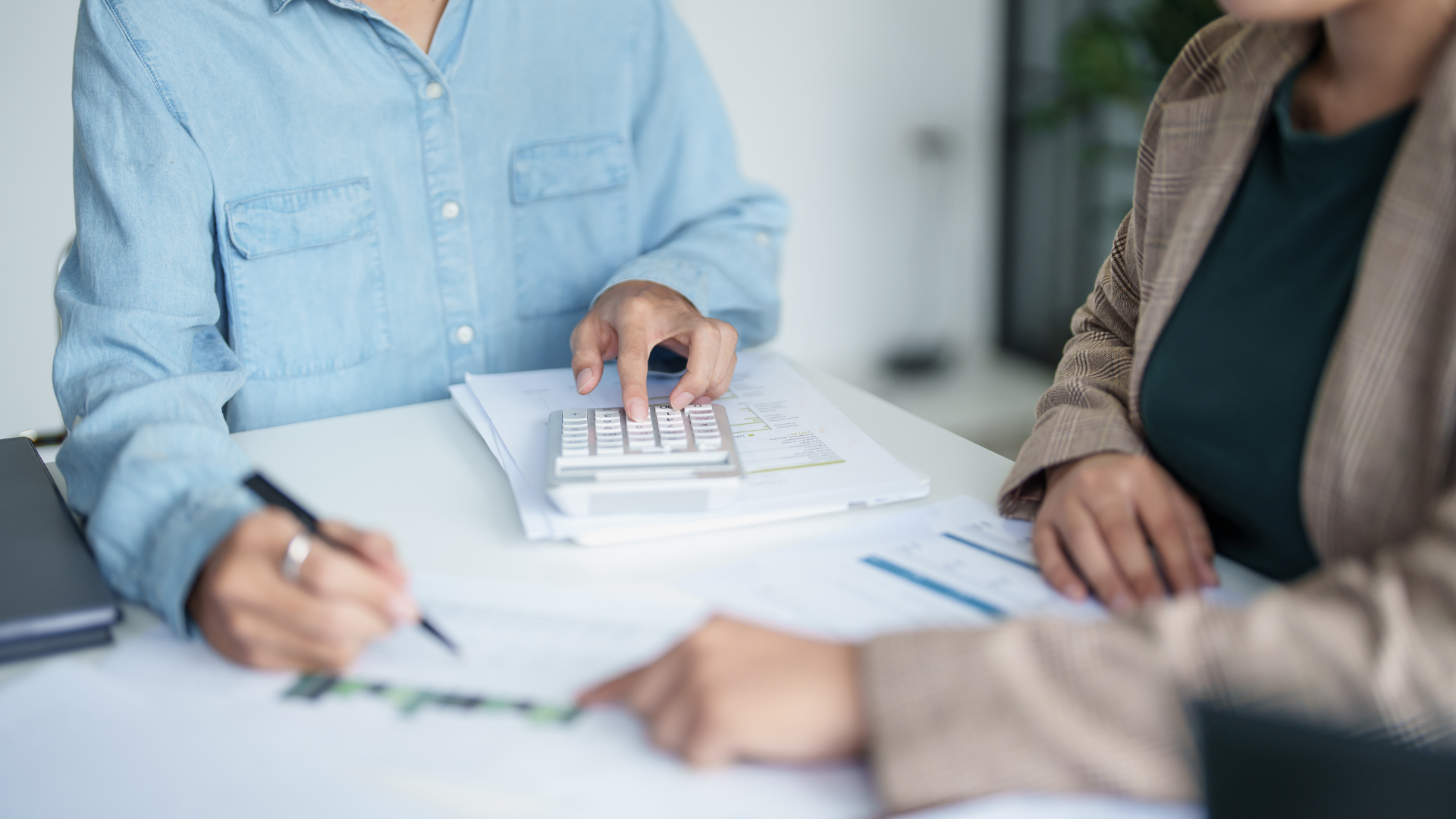 Two people review documents and write at a desk in a bright office.