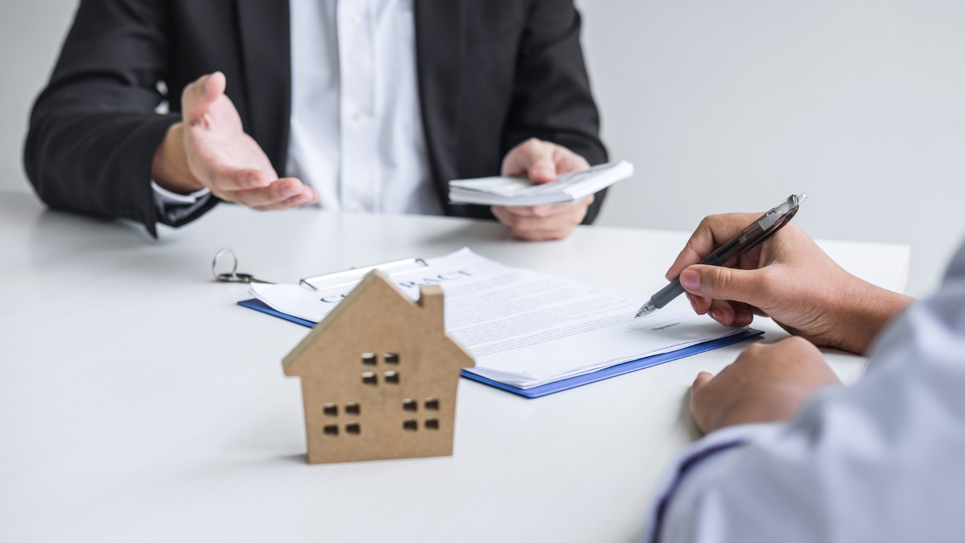 Small house model on a desk during a real estate meeting, with people discussing and taking notes