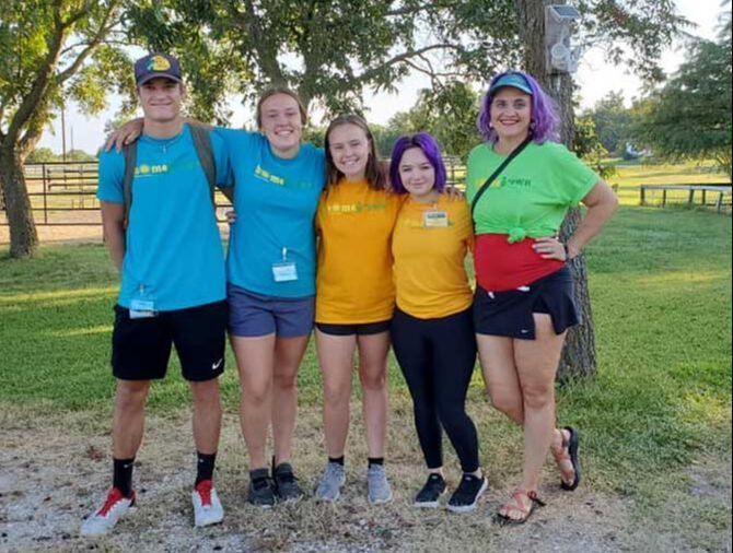 Five people posing outdoors in matching bright shirts, smiling in a grassy park.