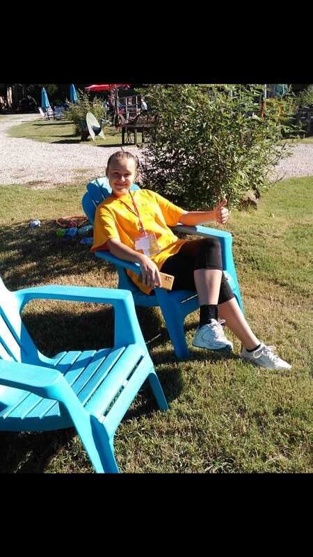 Person reclining in a blue chair on grass beside another empty chair in a sunny park