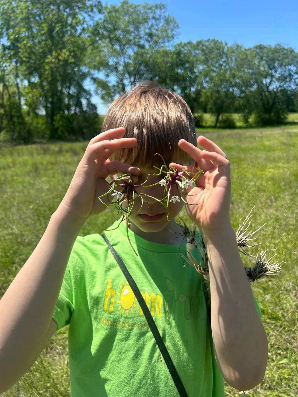 Child in a bright green shirt holding flowers up to their face in a sunny field