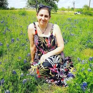 Person sitting in a sunny wildflower field, smiling in a black floral dress.
