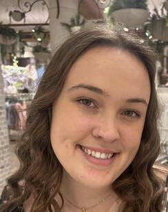 Smiling woman with wavy brown hair in a store, with plants and shelves in the background