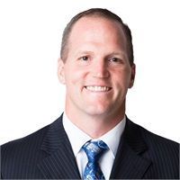 Man in a suit smiles at the camera, wearing a blue patterned tie and a white shirt.