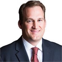 Man in a suit smiles at the camera, red tie, white shirt, dark blue jacket.