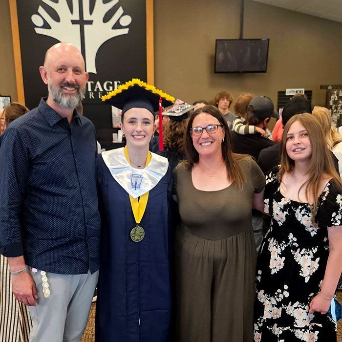 Group photo at graduation: student in cap and gown with three smiling family members indoors.