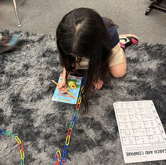 Child kneeling on a gray rug, playing with colorful link chains and a book near a puzzle board.
