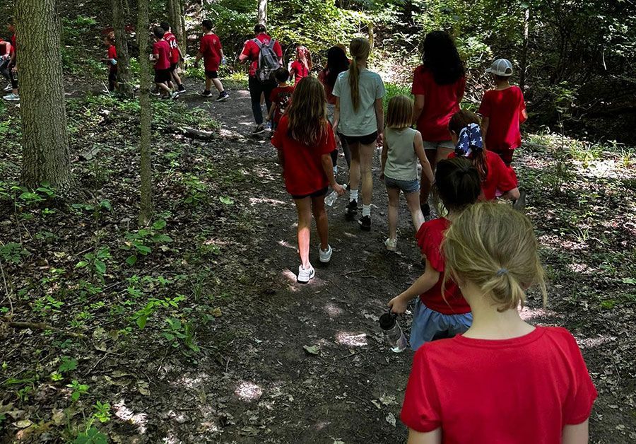 Children in red shirts walking along a wooded trail outdoors