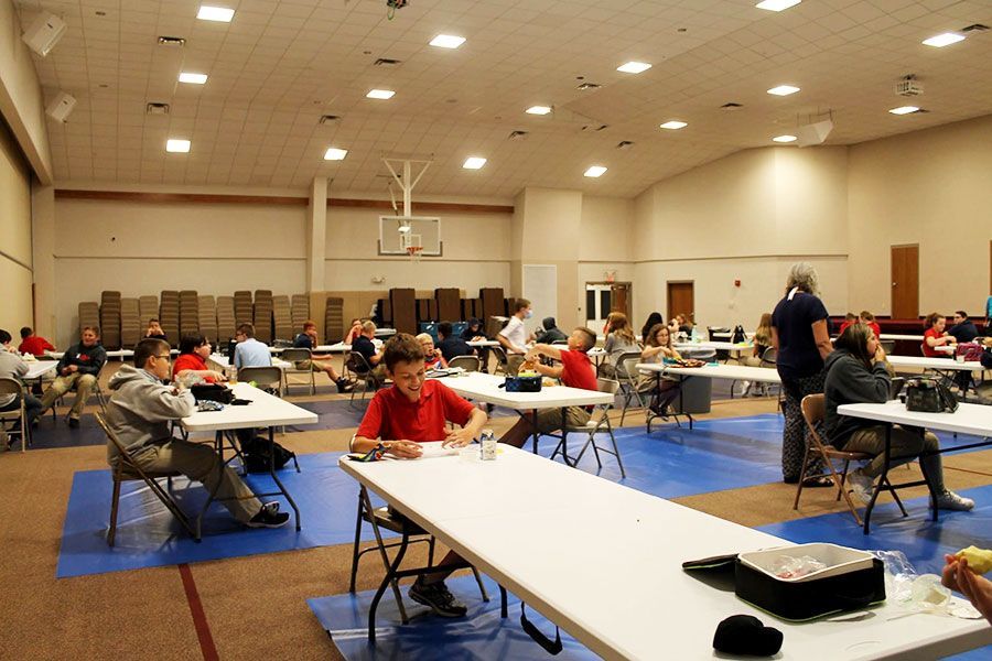 Large room with people seated at tables for a community event or meeting, with one person standing near the front.
