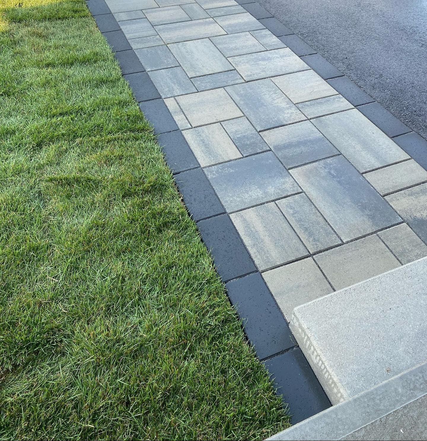 a sidewalk with a grassy border and a black border