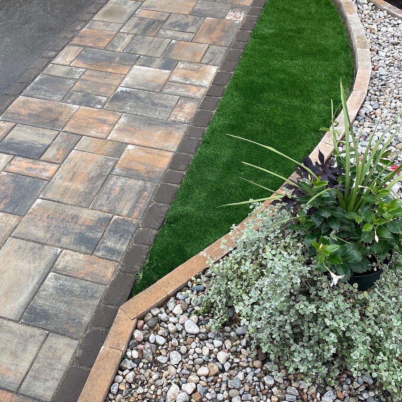 a brick walkway with grass and rocks on the side