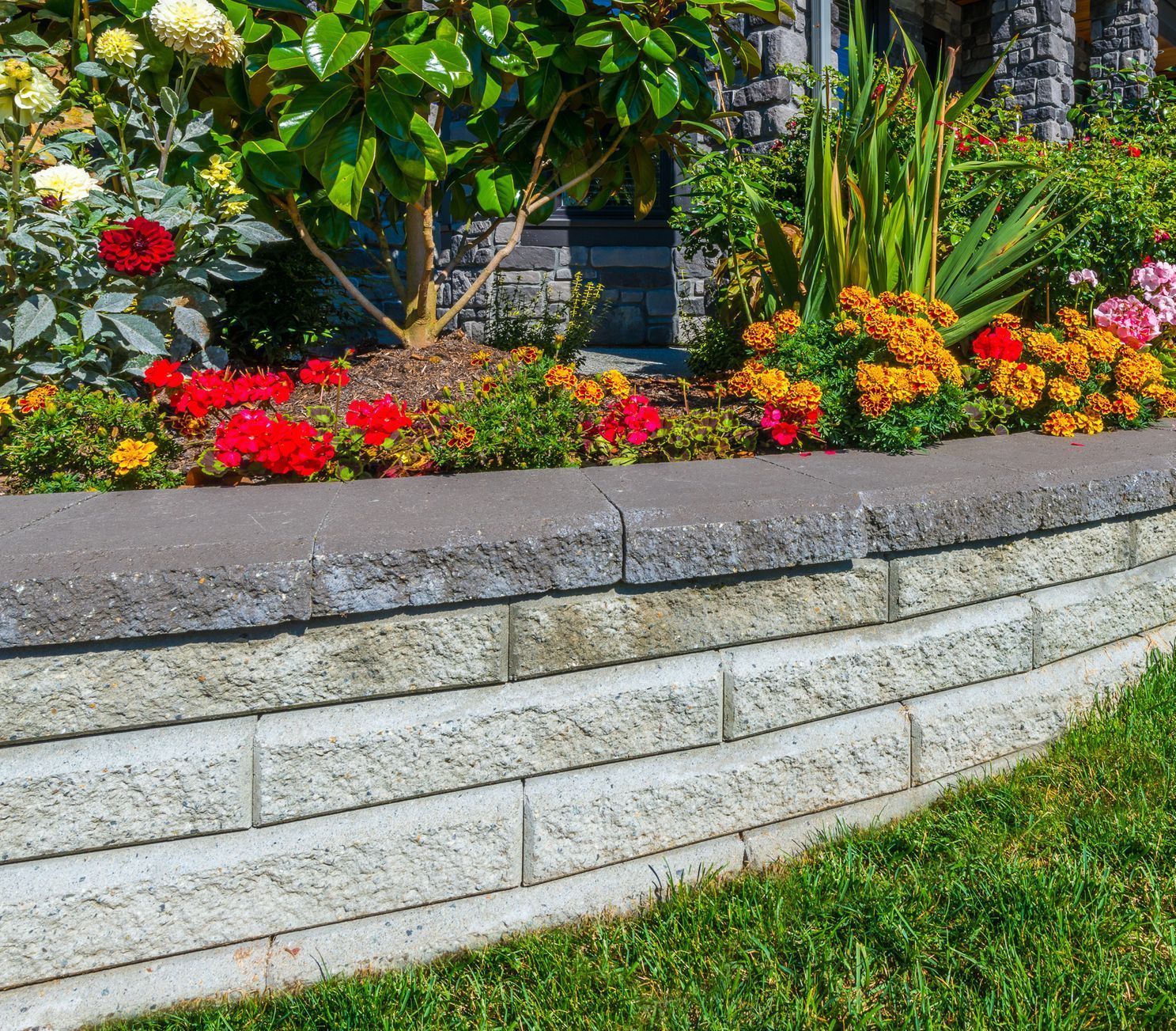 a brick wall surrounded by flowers in front of a house