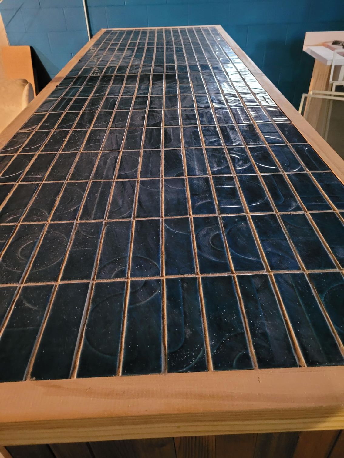 Wooden-framed solar panel with a black grid surface, shown indoors against a blue wall.