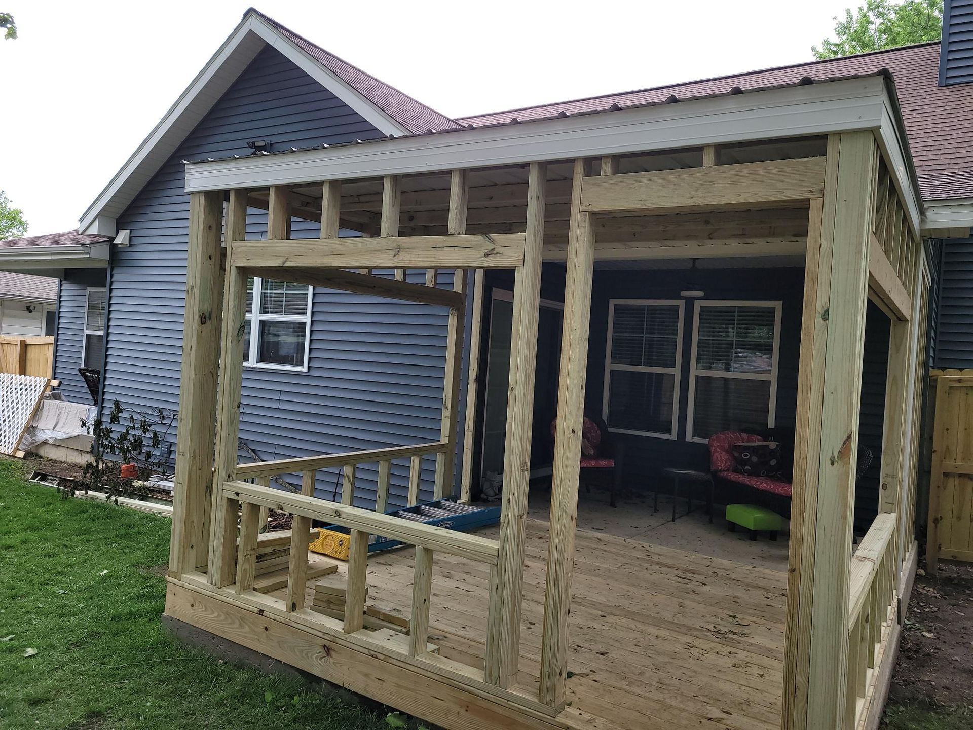 Partially built wooden porch with railing attached to a blue house in a backyard
