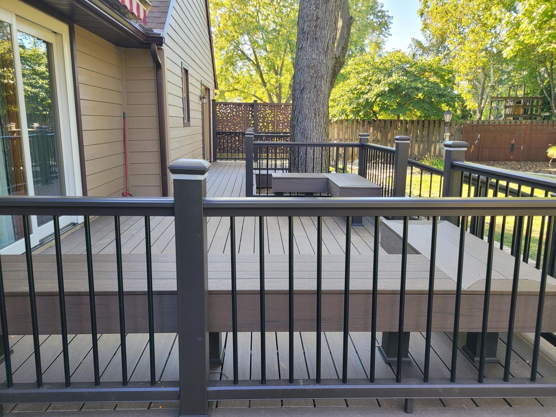 Backyard deck with black railing beside a house, overlooking trees and a fenced yard