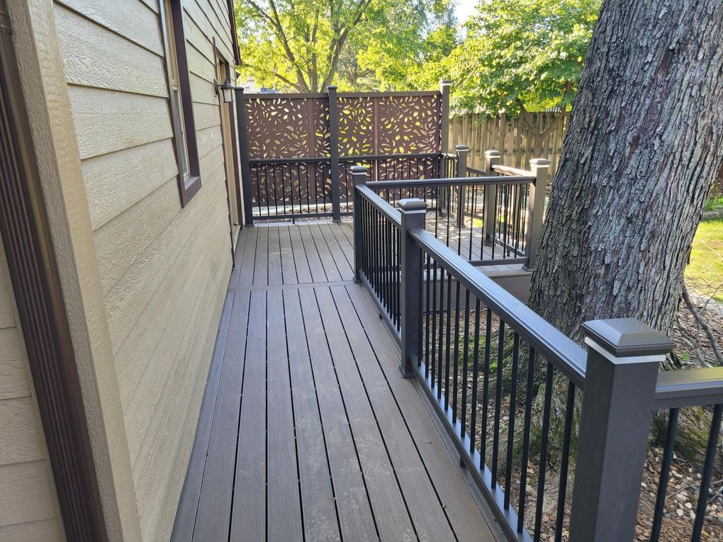 Backyard deck with red railing, beige house siding, potted flowers, and a playset in the background