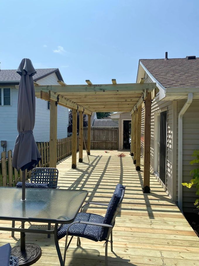 Wooden backyard pergola casting shadows on a deck with patio furniture and a closed umbrella