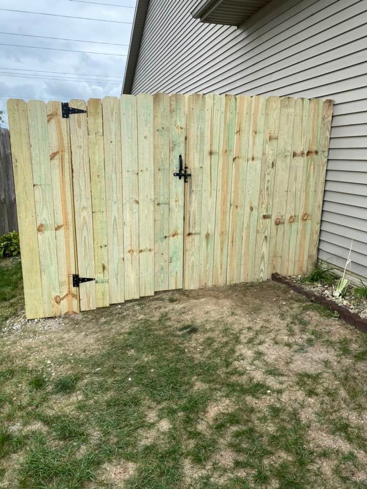 Pale wood gate in a fenced backyard beside a beige house and brick wall.