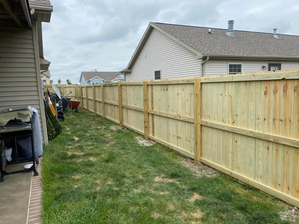 Narrow grassy side yard beside a house and new wooden privacy fence under a cloudy sky