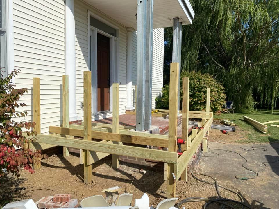 Wooden porch deck under construction beside a white house, with posts and framing in place.