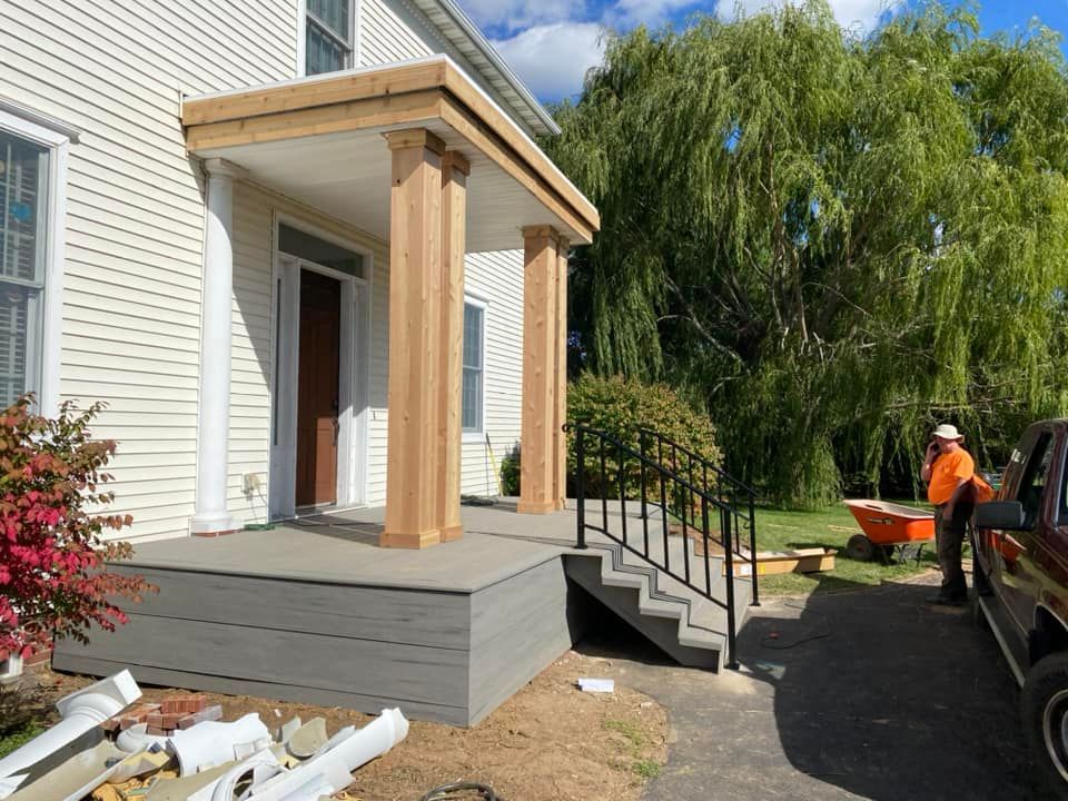 House entry porch with new steps and black railing; worker in orange safety gear by the yard.