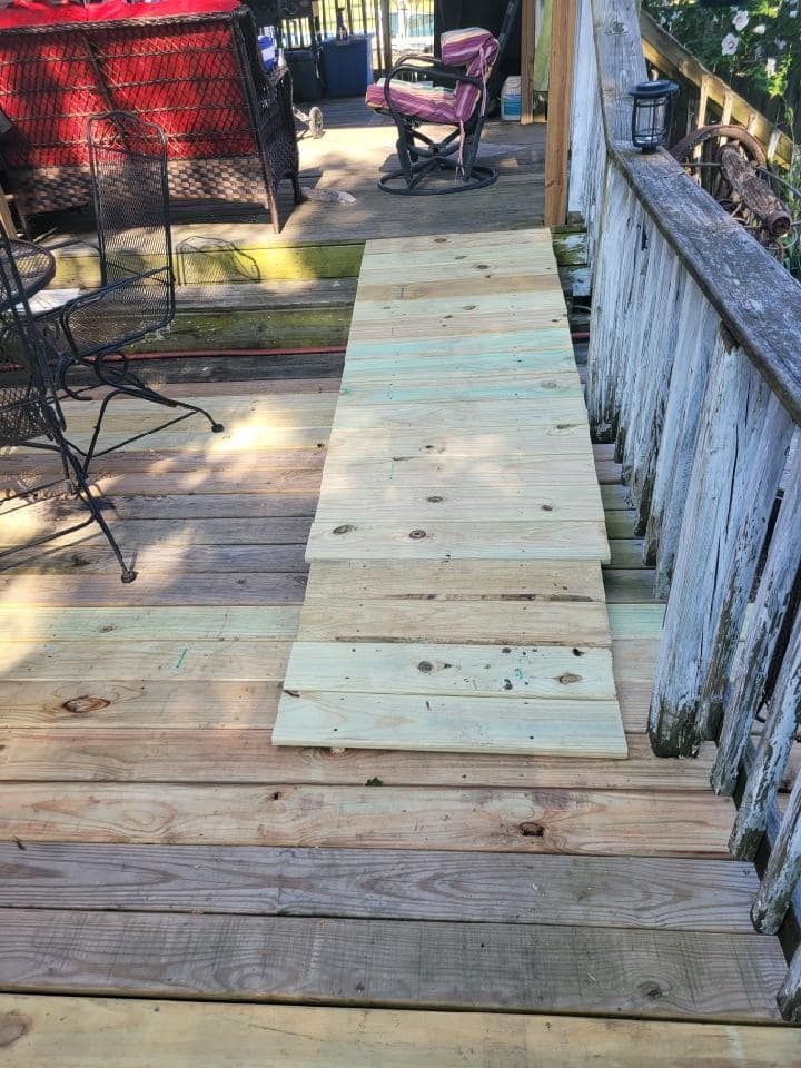 Wooden deck with a light plywood walkway board running down the center beside railings and patio chairs.