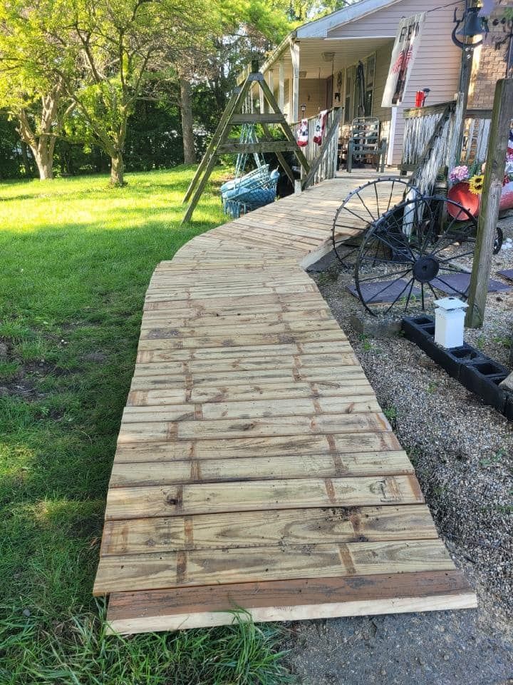 Curved wooden walkway leading to a porch beside a grassy yard and trees
