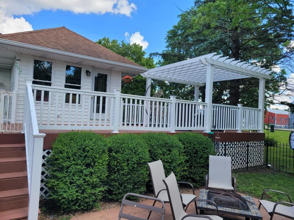 White house porch with railing, pergola, and patio chairs over a green yard under a blue sky