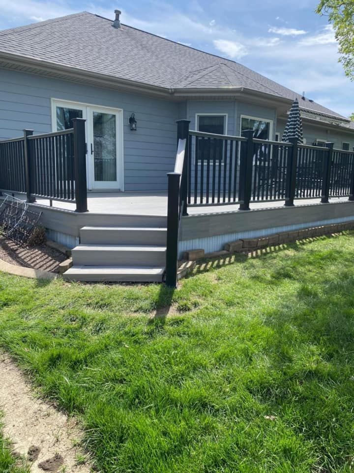 Back deck with black railings and steps leading to a gray house, overlooking a grassy yard