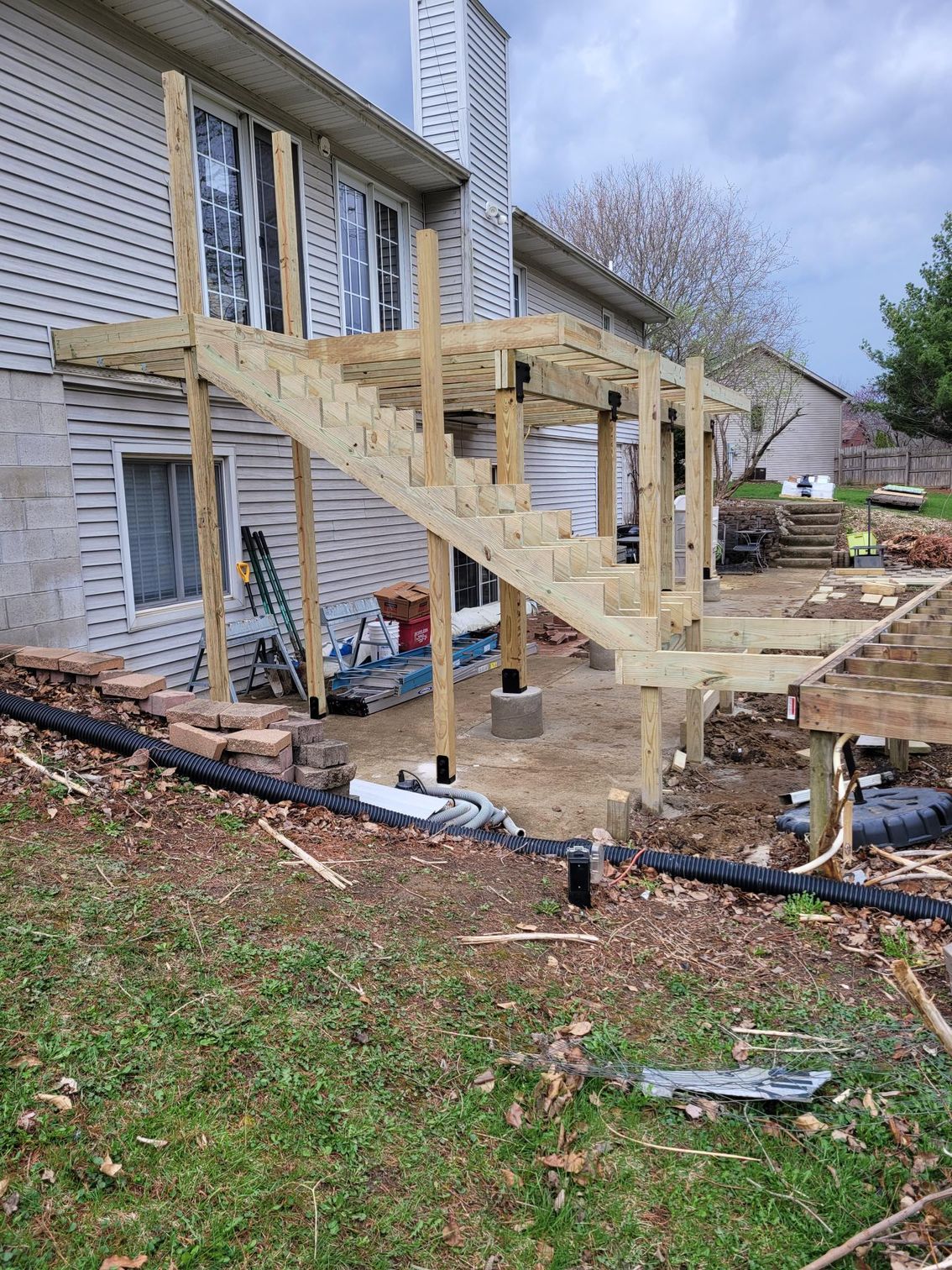 Wooden staircase under construction beside a weathered house in a yard with posts and tools.