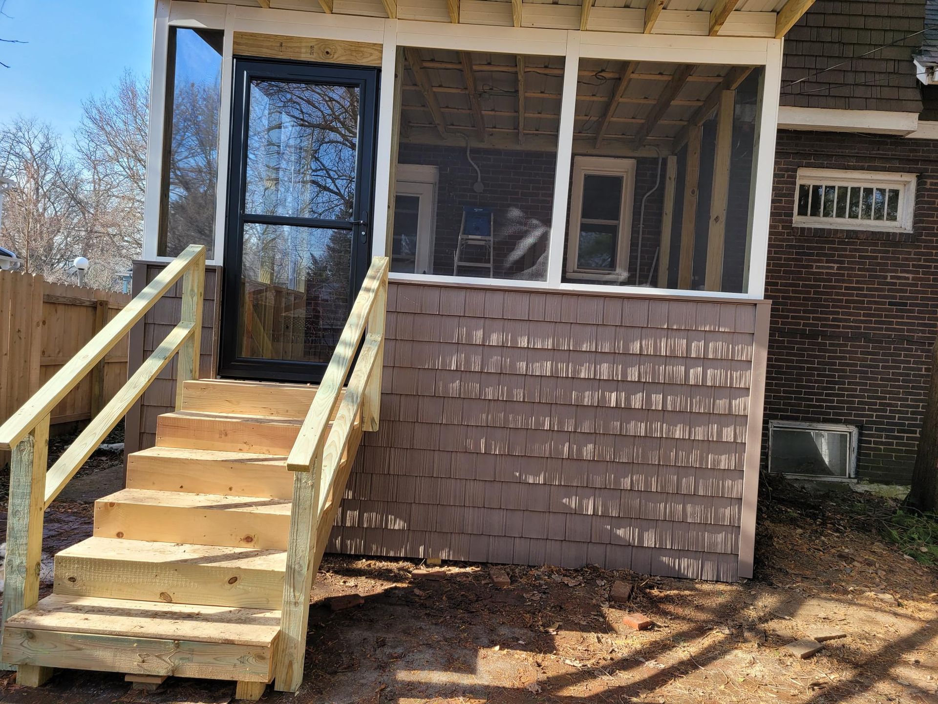 Front porch with wooden stairs and railing leading to a screened entry on a house.