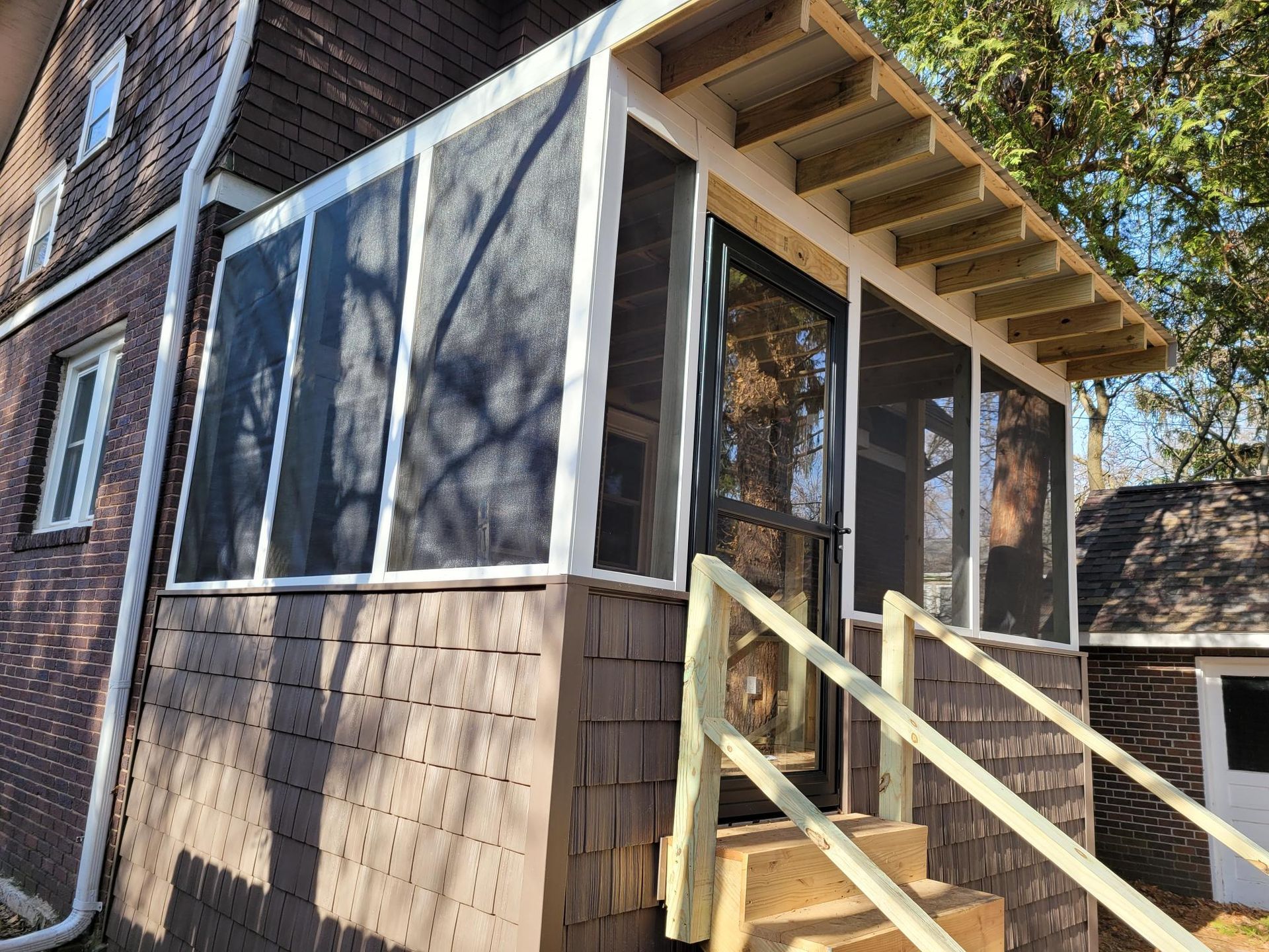 Screened porch with wooden steps and railing on the side of a house.
