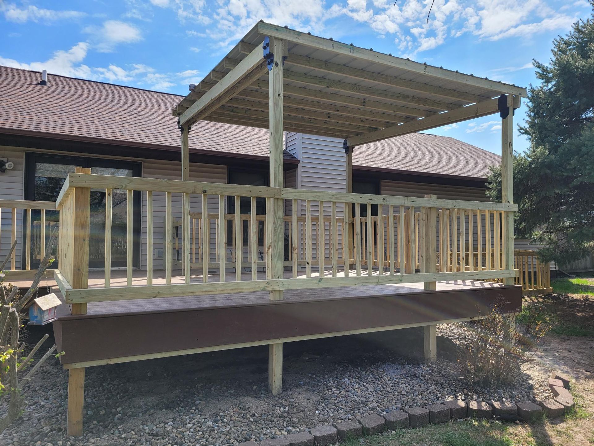 Wooden deck ramp with railing and a covered canopy beside a house