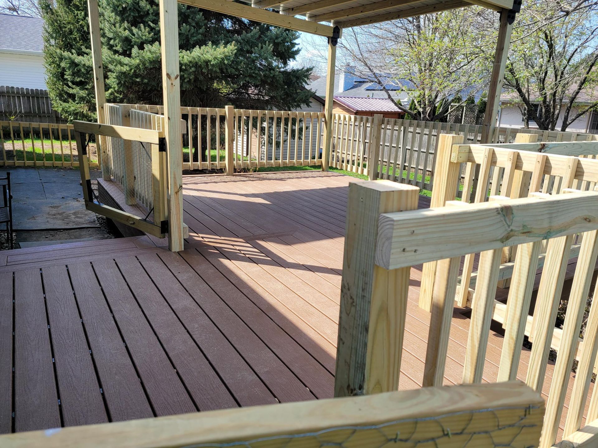 Wooden wheelchair-accessible ramp and deck with railings in a sunny backyard gazebo area