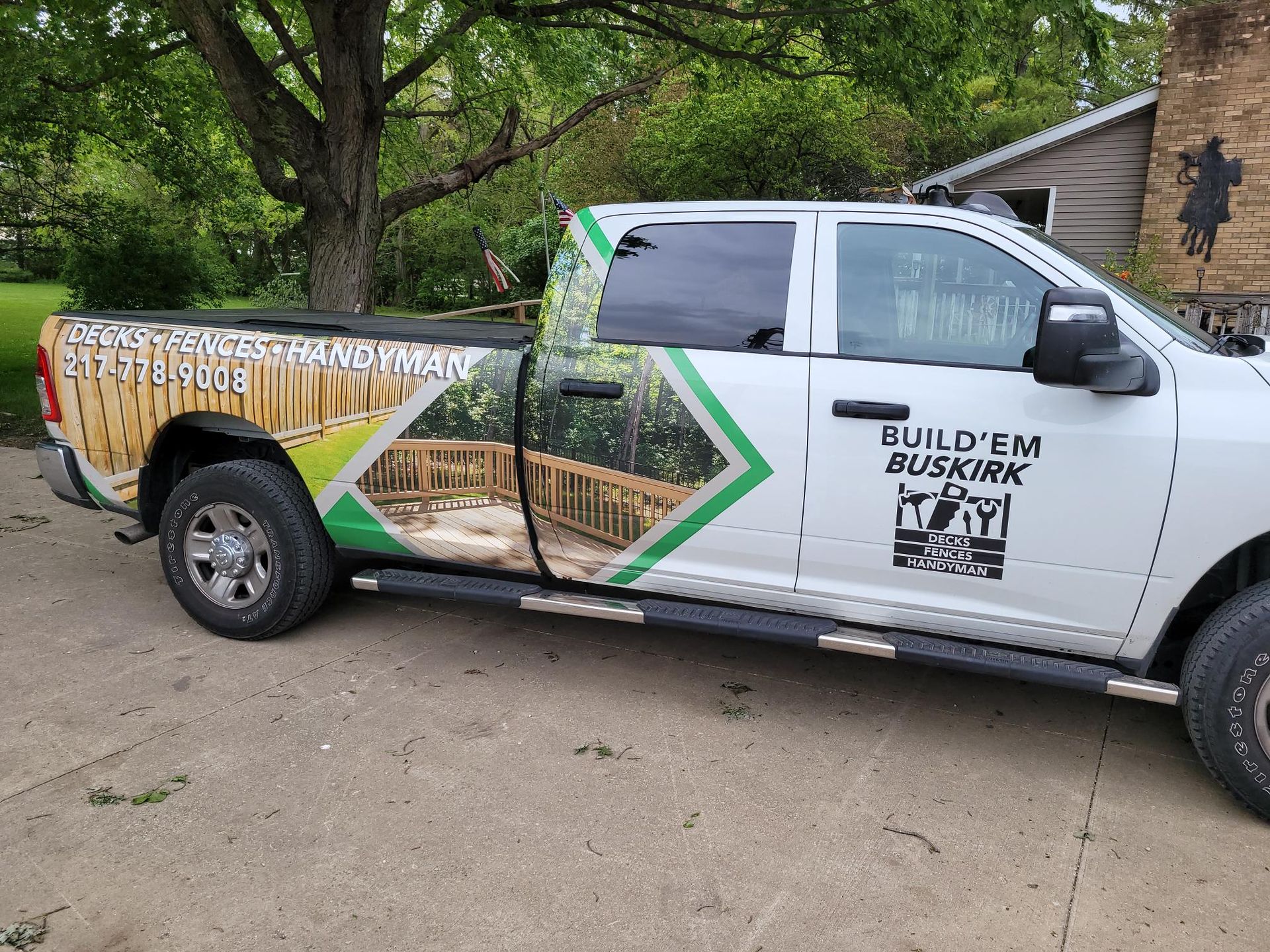 Branded pickup truck with green-and-white graphics parked by a tree-lined house driveway.