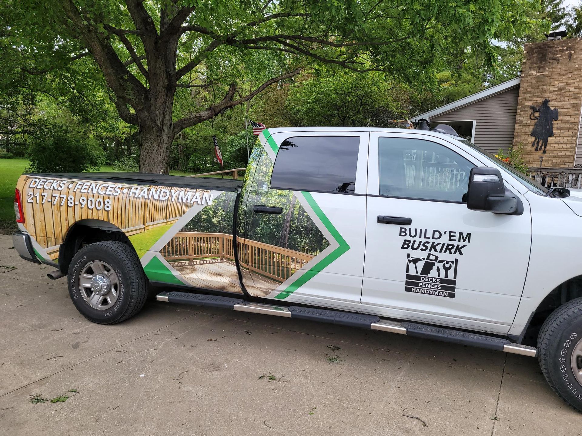 Branded white pickup truck with green geometric decals parked outdoors beside a house and trees
