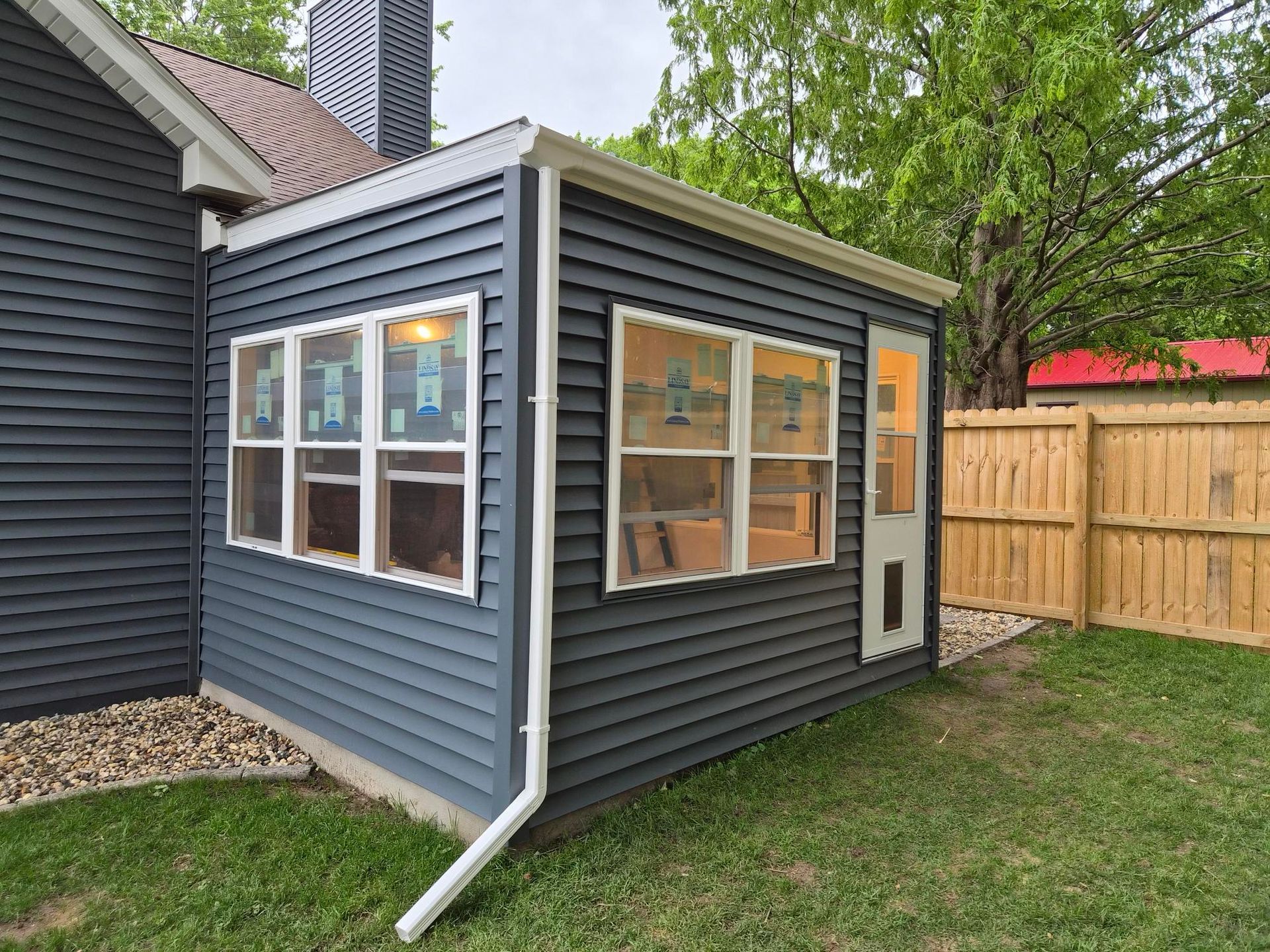 Small gray house addition with white-trimmed windows and a side door in a backyard