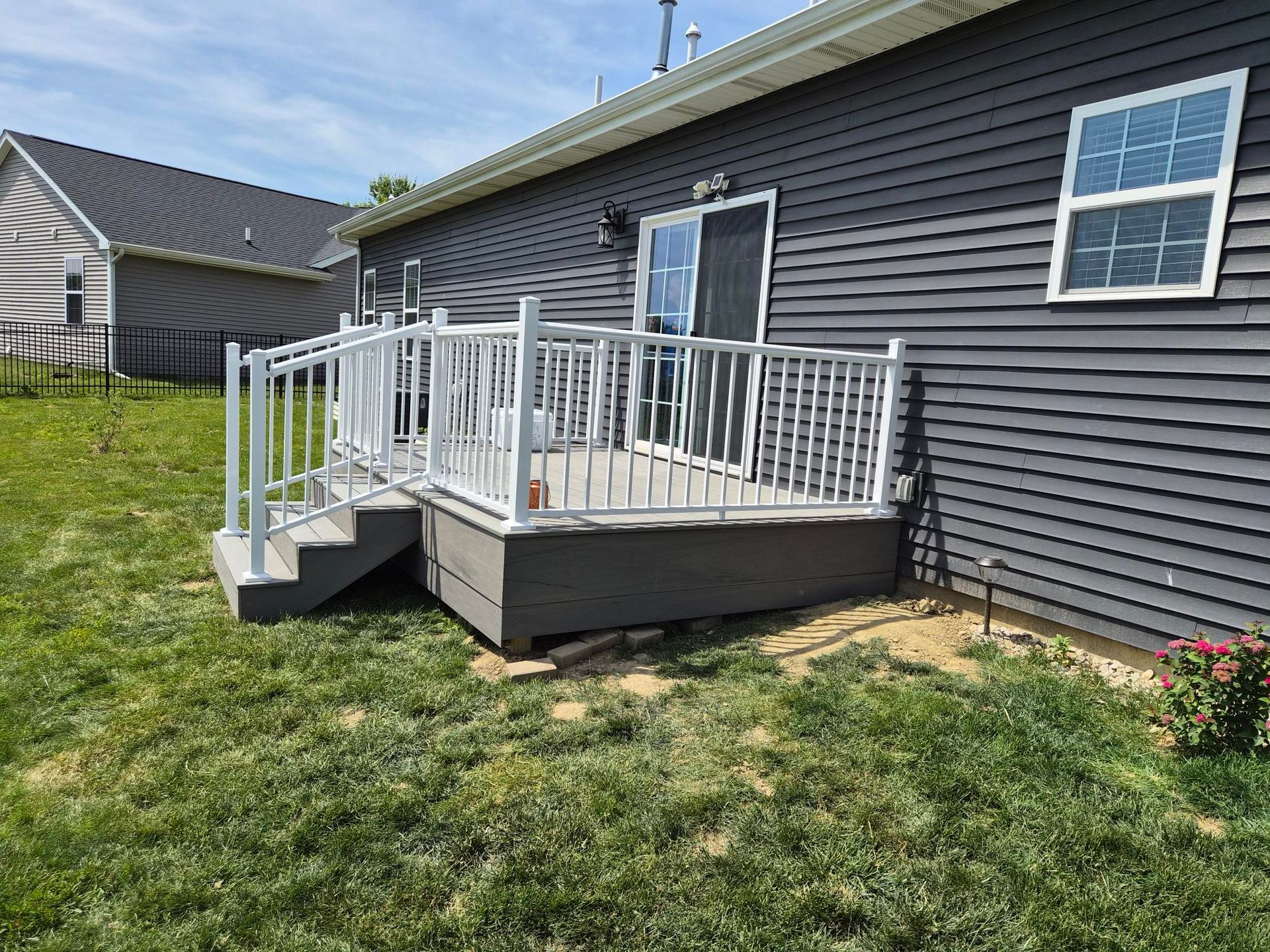 Raised wooden deck with white railings beside a gray house and grassy yard.