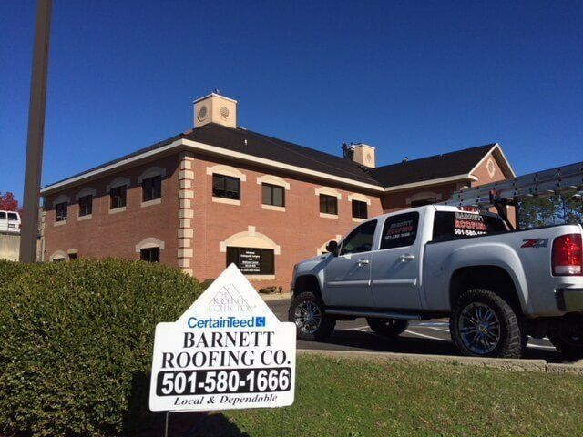A truck is parked in front of a building with a sign that says barnett roofing co.