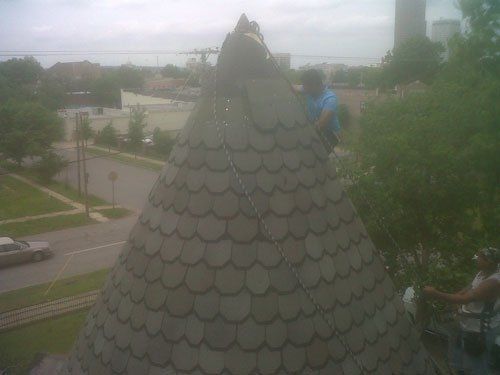 A man is standing on top of a pyramid shaped roof.