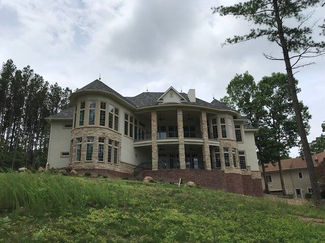 A large house is sitting on top of a grassy hill surrounded by trees.